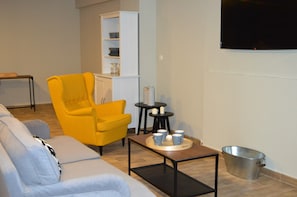 A living room with a yellow armchair, a grey sofa, a coffee table with cups, a white cabinet, and a TV on the wall. - The Hostel (Monachil)