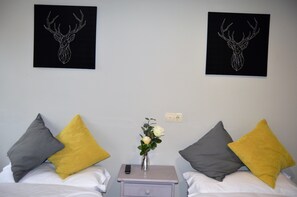 A hotel room with two beds, each with a pillow and a remote control on a nightstand. There are two framed deer antlers on the wall. - The Hostel (Monachil)