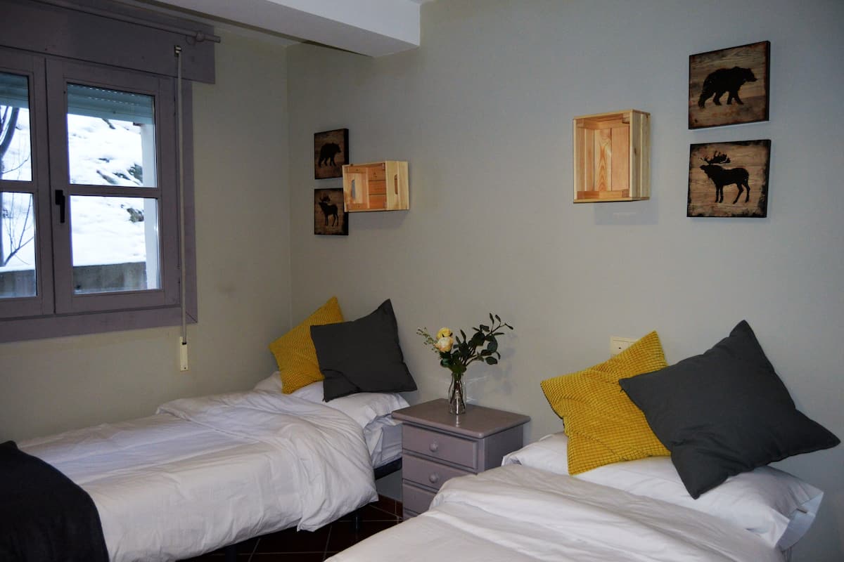 A bedroom with two beds, a nightstand, and a window.