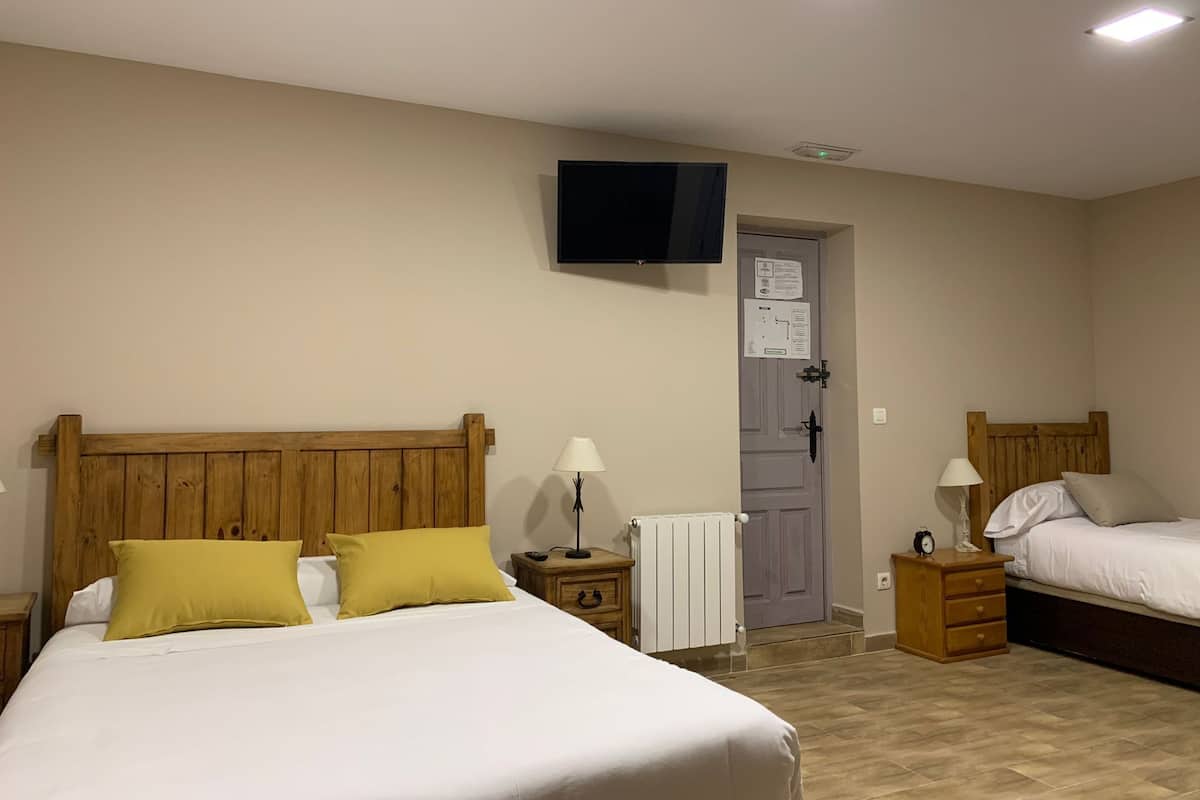 A hotel room with a large bed, two bedside tables, a wooden headboard, a television mounted on the wall, and a door with a sign.