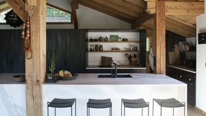 A modern kitchen with a central island, wooden beams, and a built-in shelf unit. - B&B Chalet Nono (Montriond)