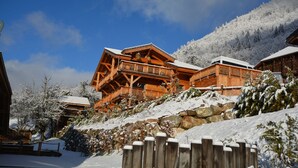 A wooden chalet with a balcony, surrounded by snow-covered trees and a mountain in the background. - B&B Chalet Nono (Montriond)