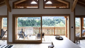 A spacious room with a large sliding glass door leading to an outdoor deck. The room features wooden beams on the ceiling and a view of a forested landscape. - B&B Chalet Nono (Montriond)