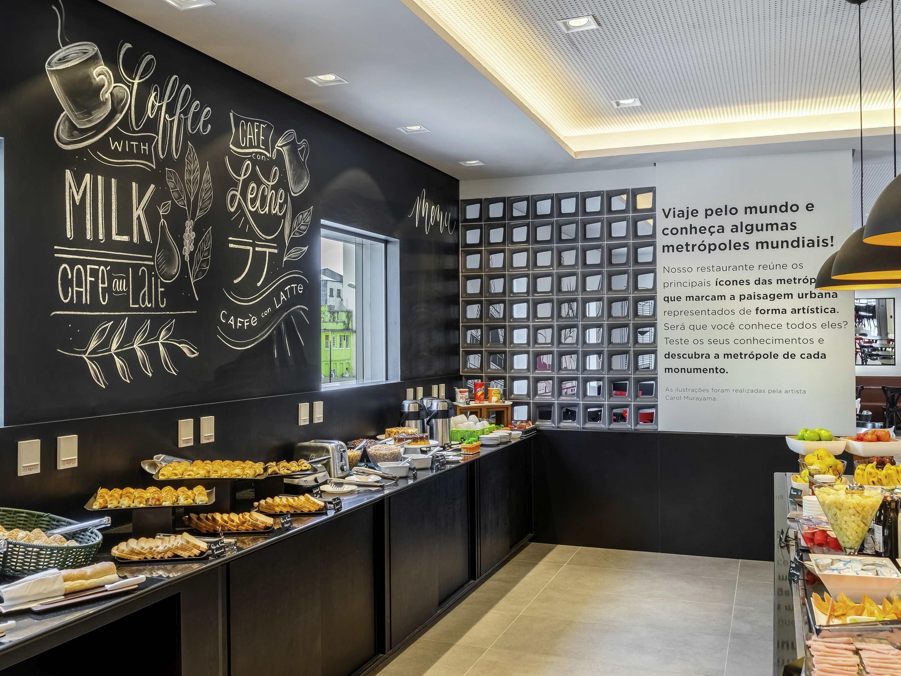 A cafe with a chalkboard wall featuring coffee and milk-related drawings, a window view, and a wall of framed pictures.