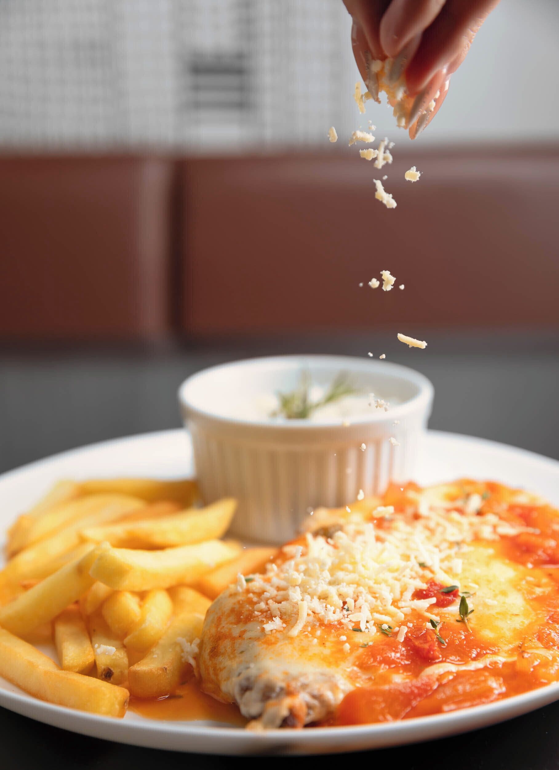 A plate of food with a baked dish, fries, and a small bowl of sauce.