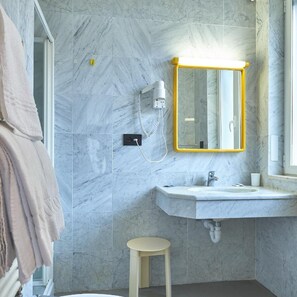A bathroom with a marble wall, a sink, a mirror, a towel rack, and a toilet. - Adler (Alassio)