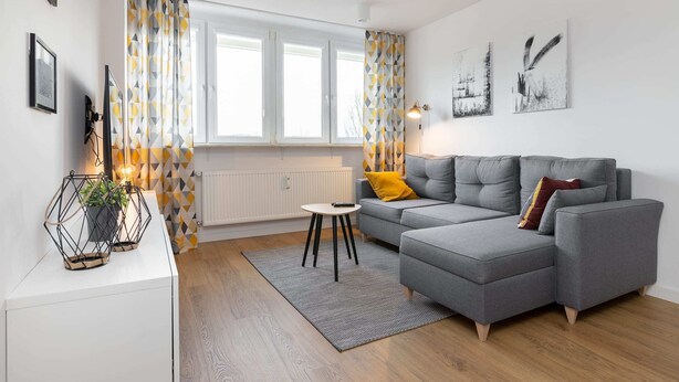 Ein modernes Wohnzimmer mit einem grauen Ecksofa, einem kleinen runden Tisch und einer Heizung.