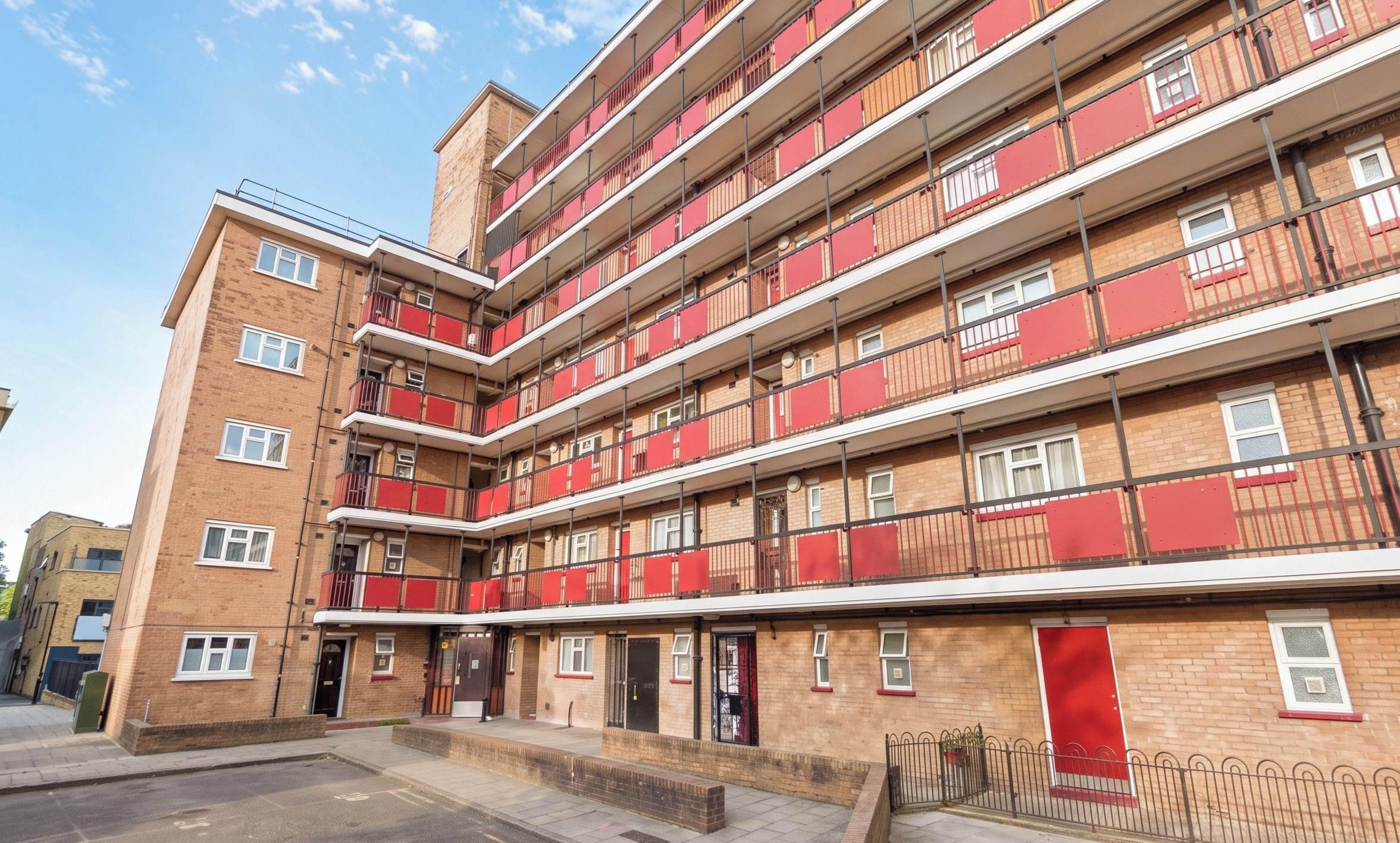 A multi-story residential building with a brick facade, multiple balconies, and a gated entrance.