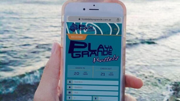Ein Smartphone zeigt eine Webseite zur Hostelerbuchung, im Hintergrund ist ein Strand zu sehen.