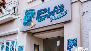 Ein Gebäude mit einem Schild, auf dem in stilisierter Schrift „PLATE“ und „plate“ steht, was auf ein Restaurant oder Café hindeutet.