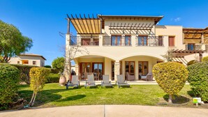 Una casa de dos pisos con un patio, mobiliario exterior y un jardín bien cuidado.