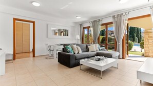 Una sala de estar moderna con un sofá gris, una mesa de centro blanca y un comedor con una mesa y sillas blancas.