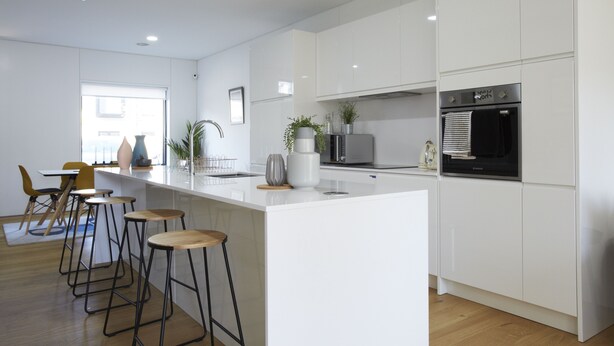 Una cocina moderna con armarios blancos, una isla central con taburetes, horno empotrado y microondas.