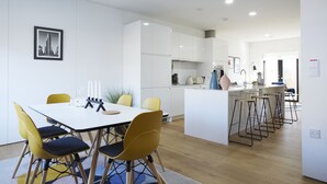 Una cocina moderna con armarios blancos, una isla central con taburetes y un comedor con sillas amarillas.