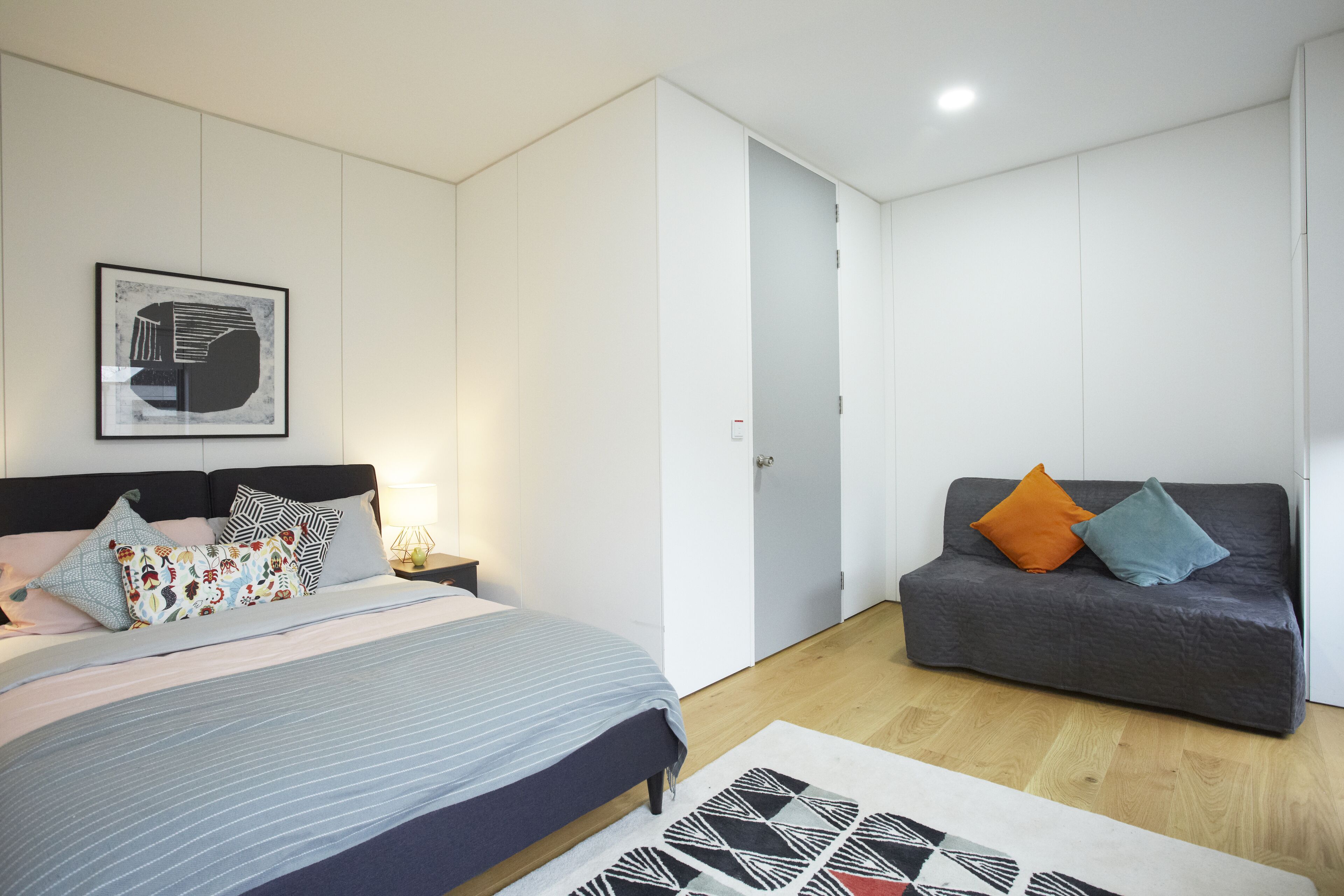 A modern bedroom with a bed, a sofa, a framed picture on the wall, and a door.