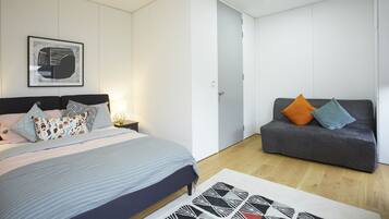 A modern bedroom with a bed, a sofa, a framed picture on the wall, and a door.