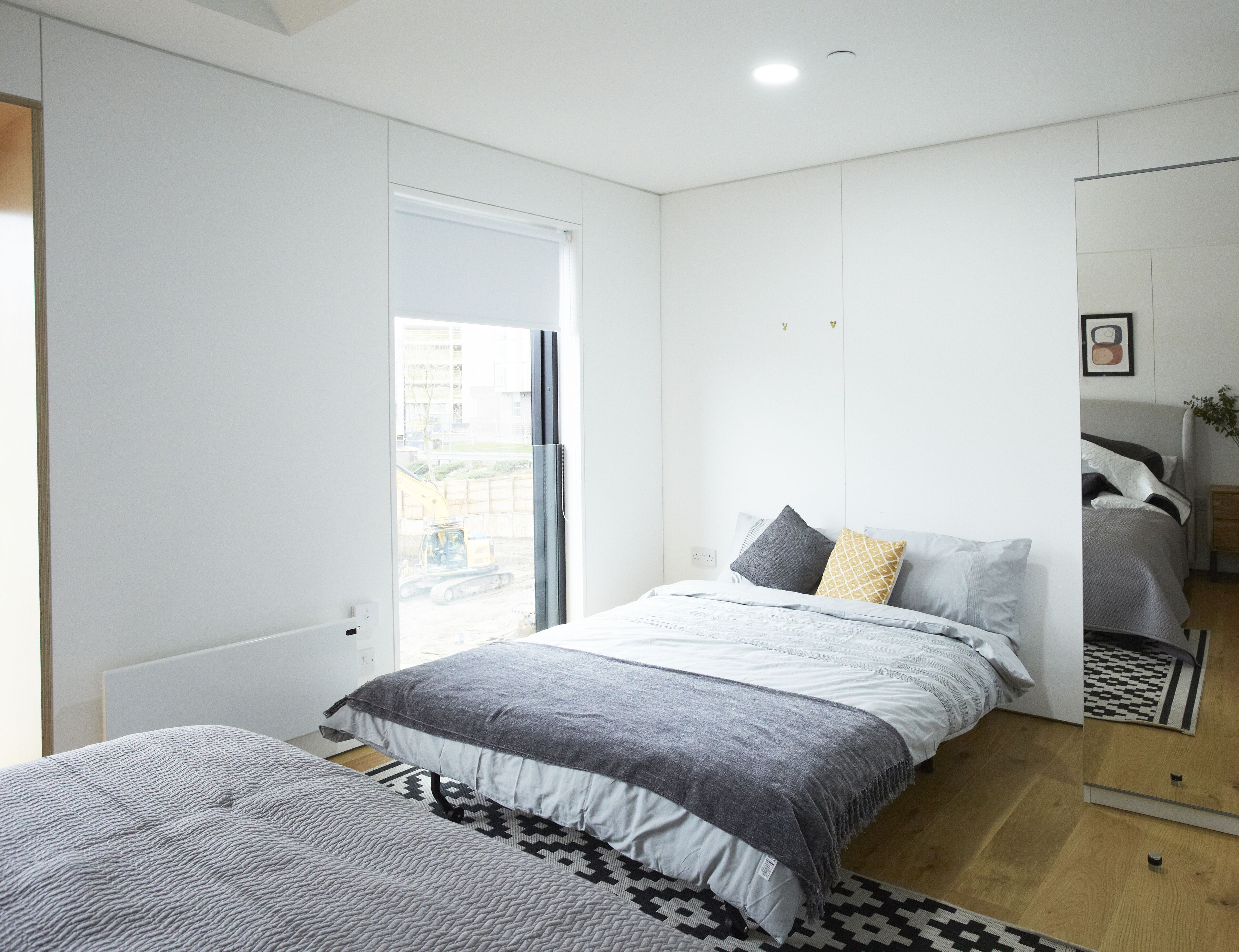 A modern bedroom with a large bed, a mirror, and a view of construction outside.