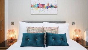 Ein Hotelzimmer mit einem Bett, zwei gemusterten Kissen, einem Stadtbild an der Wand und zwei Nachttischlampen.