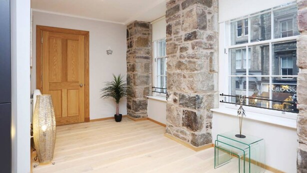 Ein Zimmer mit Holztür, Steinwänden, einem Blumentopf, einem Glastisch und einem Fenster mit Blick.
