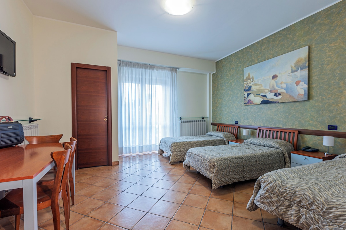 Une chambre d’hôtel avec deux lits simples, un bureau en bois avec une chaise, un radiateur et un tableau au mur.