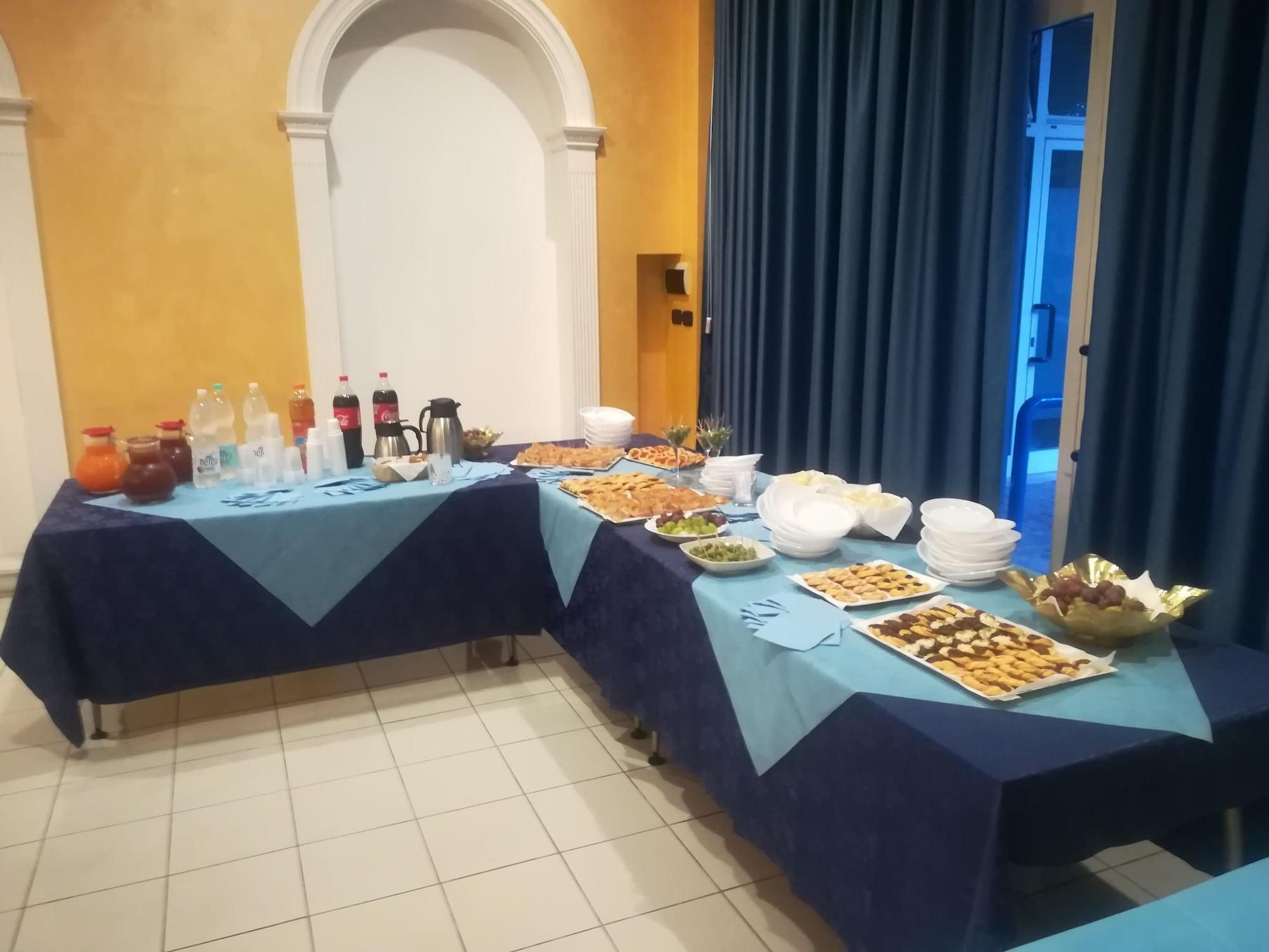 Un tavolo da buffet con diversi cibi e bevande, con a sfondo un muro giallo e un arco.