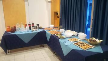 Un tavolo da buffet con diversi cibi e bevande, con a sfondo un muro giallo e un arco.
