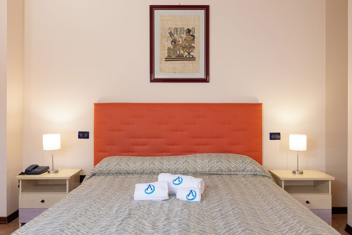 Une chambre d’hôtel avec un grand lit, deux tables de chevet, un tableau encadré au mur et deux lampes sur les tables de chevet.
