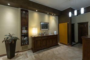 Un espace d’accueil avec un comptoir en bois, une plante en pot, un tableau encadré et un radiateur jaune.