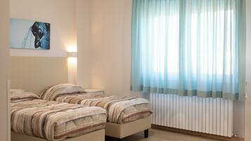 Una camera da letto con due letti, un'opera d'arte appesa al muro, una lampada da comodino e una finestra con tende leggere.