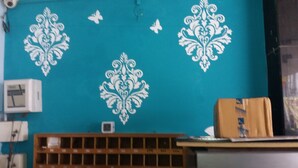 Un mur de couleur turquoise orné de motifs blancs décoratifs, une étagère en bois et un réfrigérateur portant l’inscription « Haler ».
