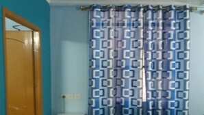 Une salle de bain avec un mur bleu, un rideau à motifs, un meuble blanc et une porte en bois.
