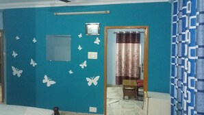 Une pièce avec un mur bleu, un ventilateur de plafond, un lit, une petite table et une chaise.