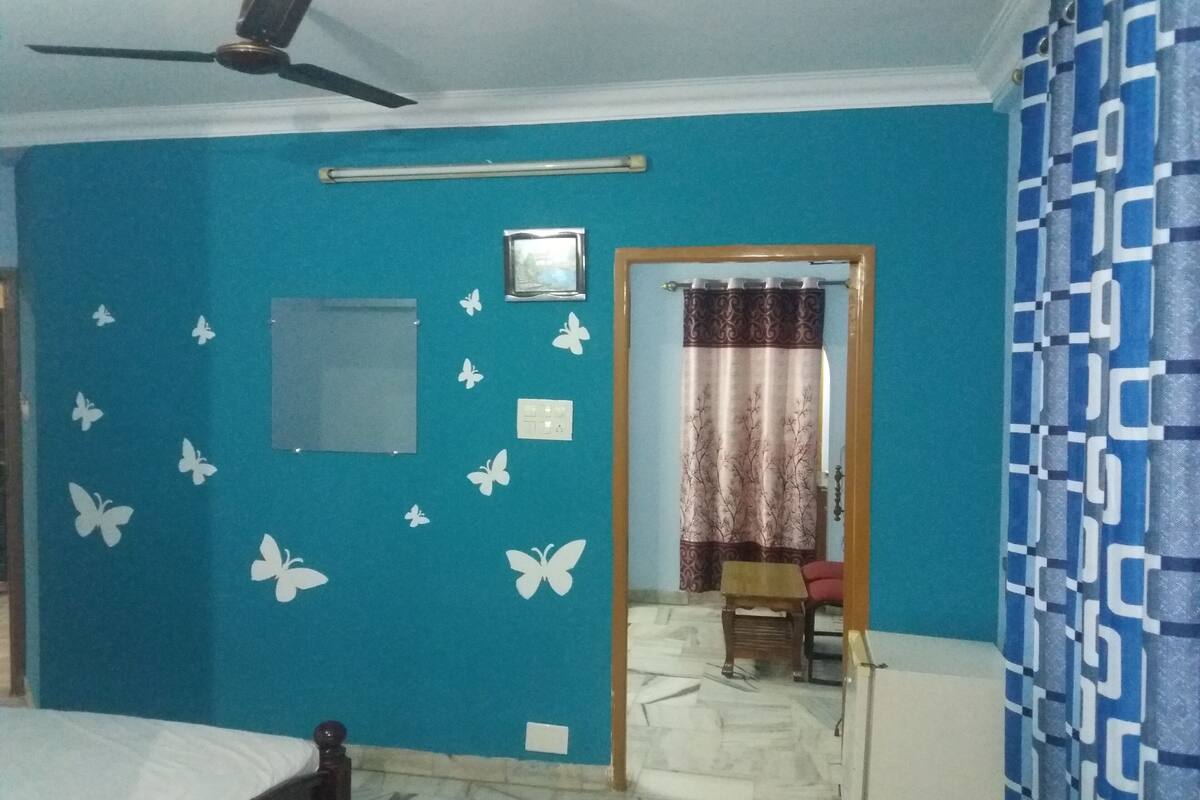 Una habitación con una cama, un ventilador de techo, una ventana, una puerta y una cortina estampada.