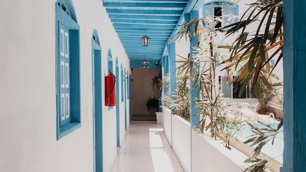 A corridor with blue-painted walls and ceiling, tiled floor, and potted plants along the right side. - Pousada Costamar (Porto Seguro)