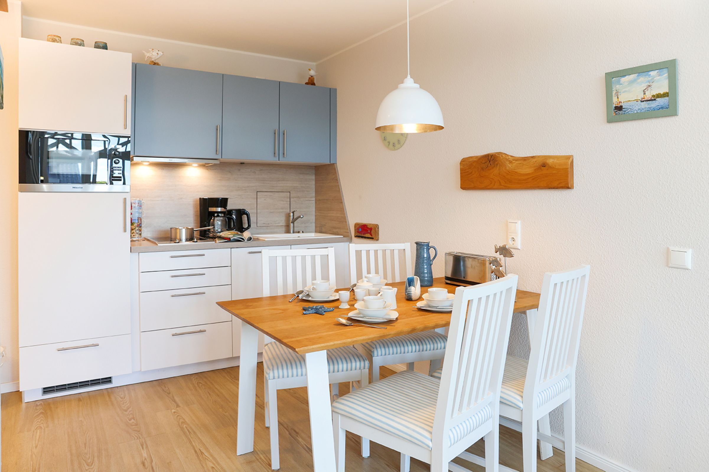 A compact kitchen with modern appliances, a dining area with white chairs, and a wooden table.