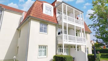 Ein zweigeschossiges Wohngebäude mit rotem Ziegeldach, weißen Außenwänden und einem Balkon im oberen Stockwerk.