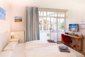 Ein Hotelzimmer mit einem Bett, einem Schreibtisch, einem Stuhl, einem Fernseher und einem Fenster mit Vorhängen.