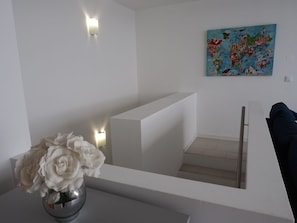 A modern interior with a white staircase, a vase of white flowers, and a colorful map on the wall.
