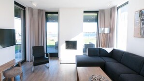 Uma sala de estar moderna com um sofá, uma poltrona, uma mesa de centro e uma televisão.