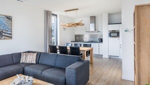 Uma sala de estar moderna com um sofá seccional cinza, uma mesa de centro de madeira e uma área de jantar com mesa e cadeiras de madeira.