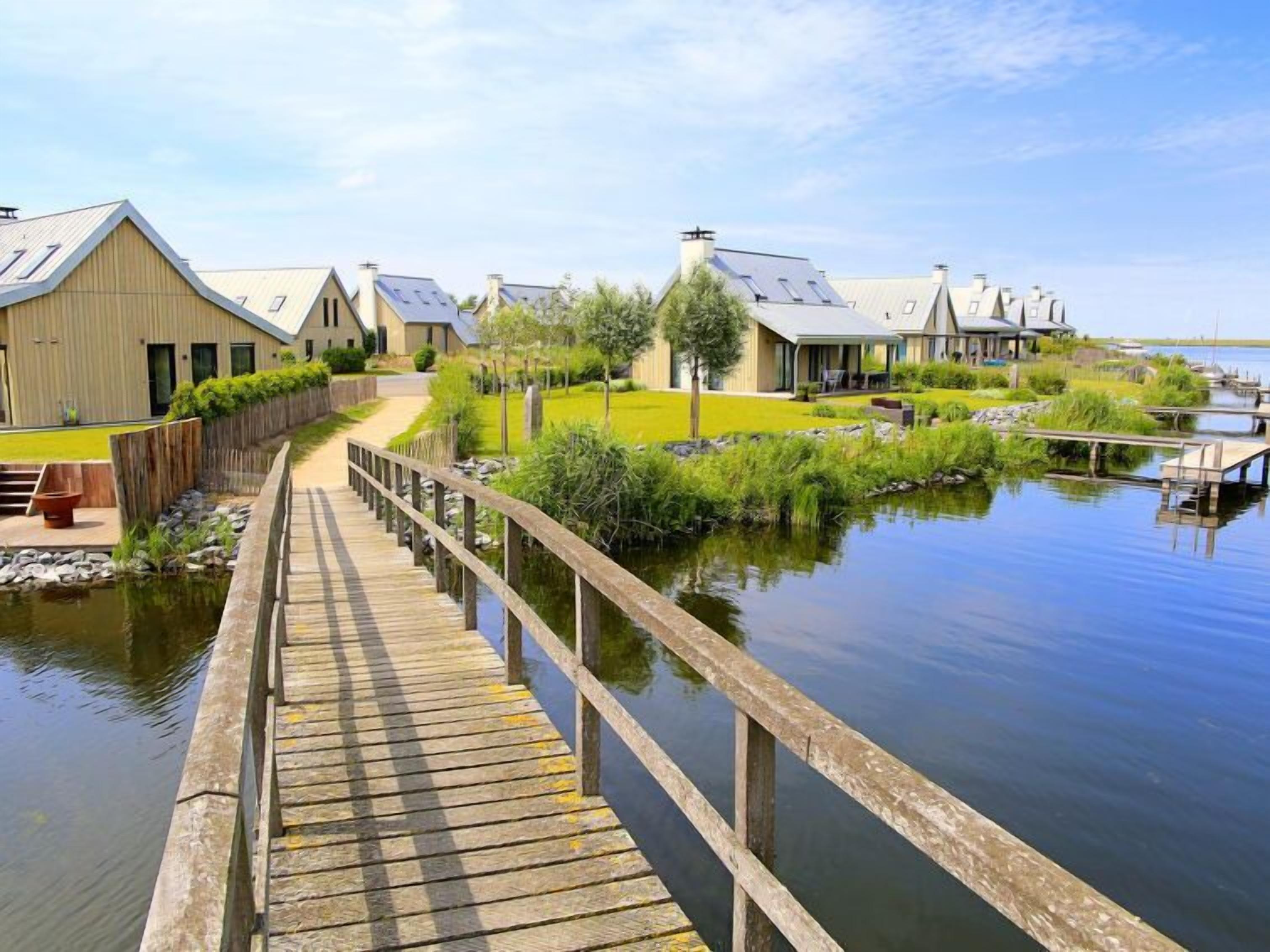 A wooden boardwalk leading to a row of modern buildings by a calm body of water.