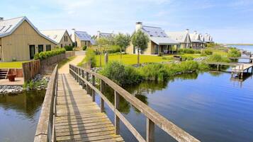 A wooden boardwalk leading to a row of modern buildings by a calm body of water.
