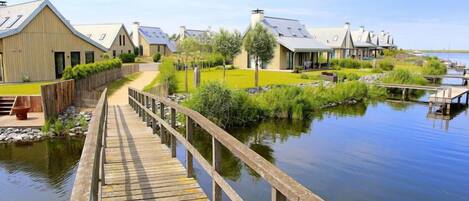 A wooden boardwalk leading to a row of modern buildings by a calm body of water.