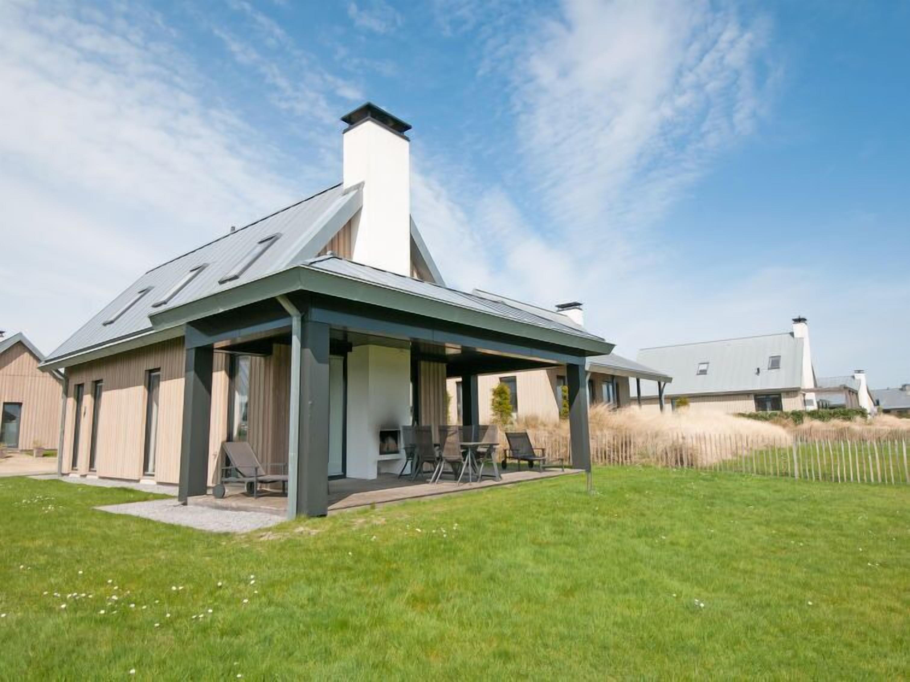 Een modern huis met een overdekte patio, een grote schoorsteen en een gazon.