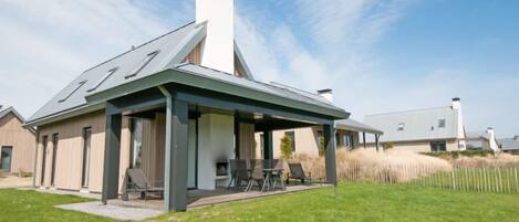 Een modern huis met een overdekte patio, een grote schoorsteen en een gazon.