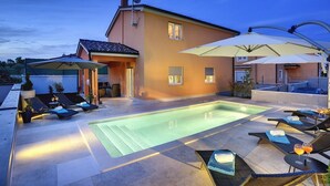 Un espace piscine avec des chaises longues et des parasols, un bâtiment équipé d’une antenne parabolique et un ciel dégagé.