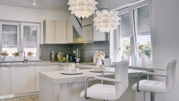 Une cuisine moderne avec un îlot central, des tabourets de bar blancs et des luminaires suspendus.