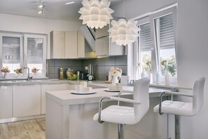 Een moderne keuken met een centraal eiland, witte barstoelen en hanglampen.