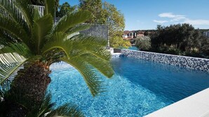 Una piscina con borde de azulejos, rodeada de vegetación y una valla.