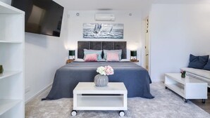 Un dormitorio moderno con una cama grande, mesitas de noche, un televisor de pantalla plana, un cuadro y un sofá.